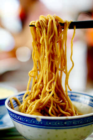 用筷子夾起的冒煙黃色麵條碗。