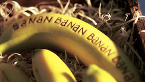 一個果皮上刻有 'BANAN' 的香蕉，藏在稻草中。 — 香蕉 壁紙