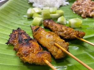 烤雞肉沙爹配青瓜和米飯放在香蕉葉上。