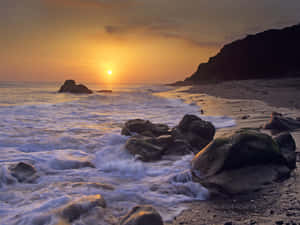 海上夕陽，海浪拍打懸崖旁的岩石海灘 — 日出 壁紙