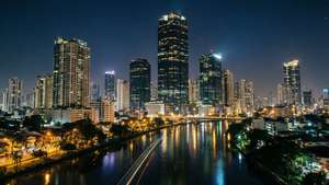夜間城市天際線，高樓大廈和閃爍的燈光倒映在河流中