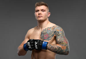 一名有紋身的男性UFC戰士戴著手套在攝影棚中嚴肅地擺姿勢。