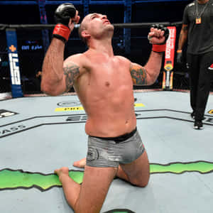 MMA拳手在八角籠中跪下，舉起拳頭慶祝勝利。