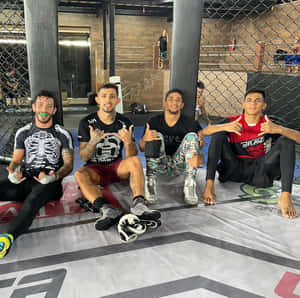 四名男性MMA拳手在健身房的籠墊上擺姿勢。