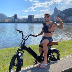 有紋身的男士在水邊騎電動單車，背景有城市和山脈 — 湖 壁紙