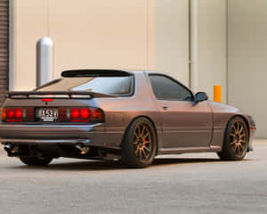 青銅色日產240SX跑車，紅色尾燈，停在米色建築附近。