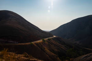 黃昏時分，一條蜿蜒的道路穿過陽光明媚的山丘，帶有鏡頭光暈