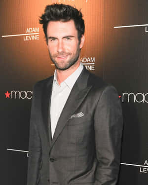 Adam Levine 在 MAC 活動中穿著灰色西裝，背景溫暖明亮。 — 4:5 壁紙