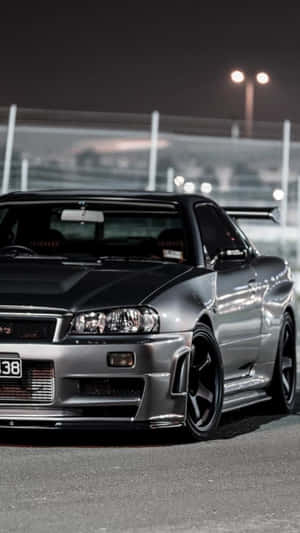 銀色日產Skyline R34在夜間賽道上，在明亮燈光下。