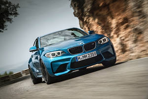 藍色BMW M2 Coupe在山路上疾馳，帶有模糊動態效果。