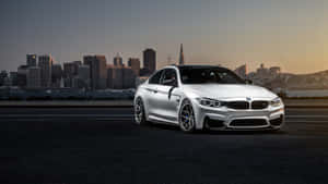 銀色BMW M4跑車停在高速公路上，背景是三藩市日落時分的天際線。