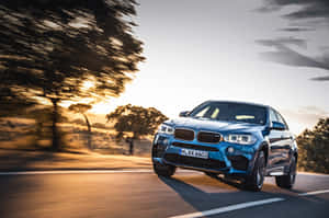 藍色BMW X6 M在日落時分在道路上飛馳，背景是模糊的樹木。 — 寶馬X6 M 壁紙