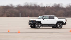 白色Hummer EV電動皮卡車在測試跑道上穿過橙色錐體行駛。 — 汽車 壁紙