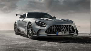 多雲天空下混凝土上的銀色 Mercedes-AMG GT Black Series 跑車。