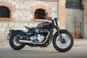 經典栗色 Triumph 電單車停泊在磚石建築前。