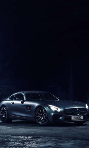銀色 Mercedes-AMG GT 跑車在黑暗的鵝卵石街道上被車頭燈照亮。