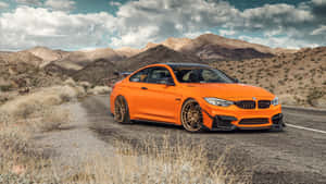 橙色BMW M4跑車在沙漠公路上，背景有山脈。