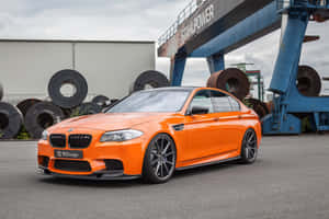 橙色BMW M5停放在工業場地，有鋼卷和藍色起重機。