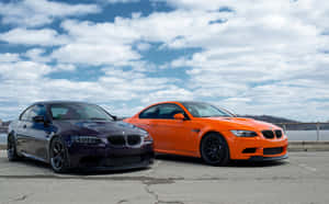 兩輛高性能BMW M3汽車並排停放在瀝青停車場上，天空多雲。