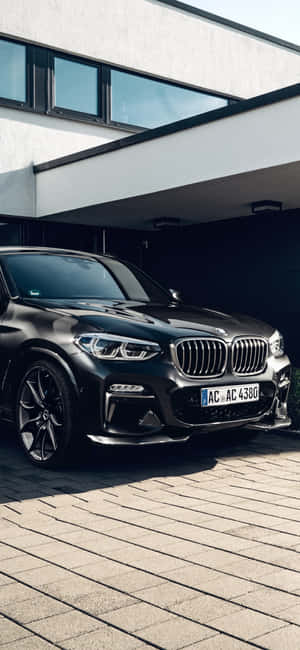 黑色BMW X5停泊在現代房屋前的石頭車道上。 — Xiaomi 14 壁紙