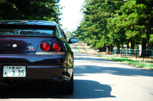 黑色日產Skyline R34停泊在陽光明媚、綠樹成蔭的道路上。 — 汽車 壁紙