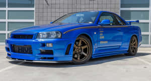 藍色日產Skyline R34 GT-R停在玻璃建築前。