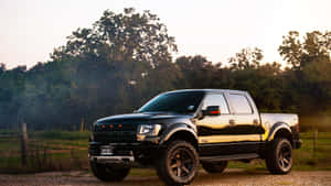 日落時分停在碎石路上的黑色升高福特F-150皮卡車，背景有樹木。