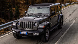 黑色Jeep Wrangler在彎曲的林間道路上行駛，帶有模糊的動態效果。