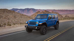 藍色Jeep Wrangler在沙漠公路上行駛，背景有山脈和日落。