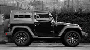 黑色Jeep Wrangler停在磚牆和灌木叢附近的街道上。