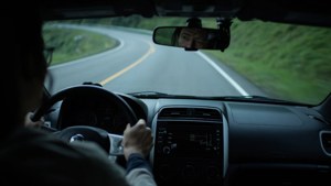 在黃昏時分駕駛汽車在蜿蜒的山路上行駛的人，綠色山坡