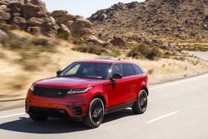 紅色Range Rover SUV在沙漠公路上行駛，地形多石。