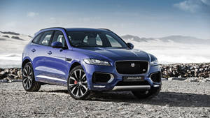 藍色Jaguar F-Pace SUV停泊在靠近雪山嘅岩石海灘上。
