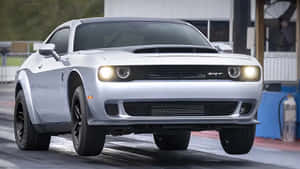 銀色Dodge Challenger SRT在潮濕的直線加速賽道上亮著車頭燈加速行駛。