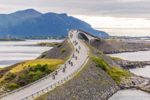 電單車手沿著風景優美的海岸道路行駛，背景有山脈和水域。 — 道路 壁紙