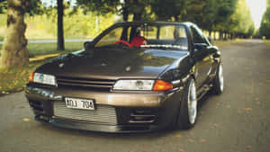 黑色日產Skyline R32停泊在落葉滿地的道路上，背景有樹木。