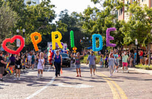 人們在陽光明媚的街道上用巨大的彩虹氣球字母拼出PRIDE和一個心形來慶祝Pride。