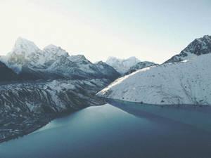 白雪覆蓋的山峰在晴朗的天空下倒映在平靜的藍色湖泊中。 — 冬天桌面 壁紙