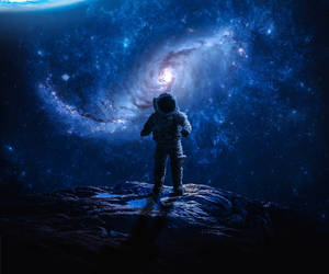 一名孤獨的太空人在岩石行星上欣賞深空中發光的螺旋星系。 — 太空 壁紙