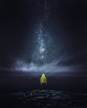 穿著黃色外套的人站在岩石上，星空下銀河可見
