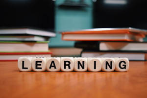 白色字母骰子拼出 learning，放在木桌上，後面有書本。
