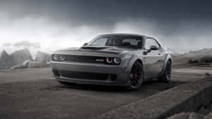 灰色 Dodge Challenger SRT Hellcat 停泊在混凝土上，背景有暴風雨的天空和岩石。