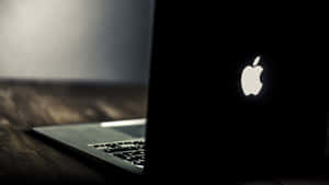 帶有發光Apple標誌的銀色手提電腦在深色木質表面上