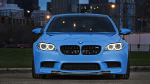 藍色BMW M5夜間停泊在城市中，車頭燈亮起。