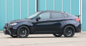 黑色BMW X6M運動型SUV停靠在青綠色金屬牆旁。 — 寶馬X6 M 壁紙