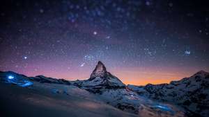 白雪覆蓋的山峰在紫色和橙色色調的星空暮色天空下。