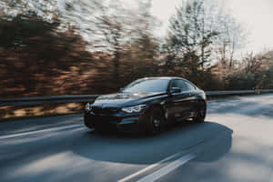 日落時分，黑色BMW M4雙門跑車在森林道路上飛馳。