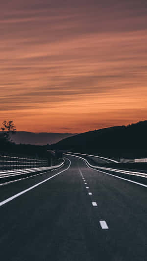 日落時分的彎曲道路，橙色天空和暗色山丘