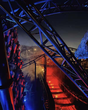 夜間以紅藍燈光照亮的過山車軌道，下方有薄霧。 — 4:5 壁紙