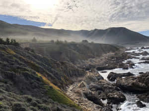 在明亮的陽光下，海岸懸崖伴隨著拍岸的浪花和霧氣籠罩的山丘。